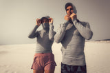 ION Rashguard Sun Pro SS26 mit Kapuze in Grau, langärmelig, am Strand getragen, Frontalansicht von zwei Personen