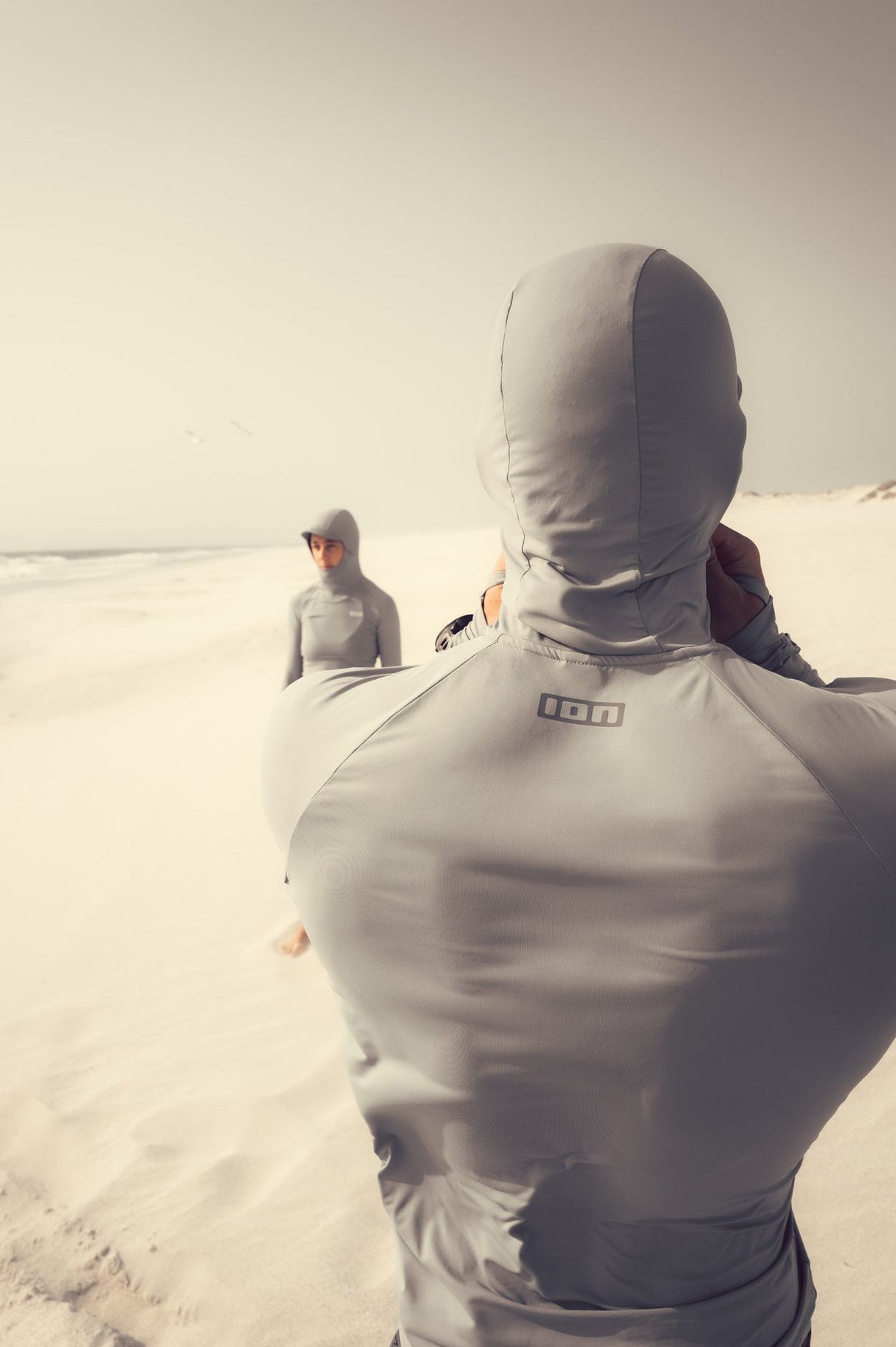ION Rashguard Sun Pro SS26 grau mit Kapuze, Rückansicht am Strand, UV-Schutz Sportbekleidung