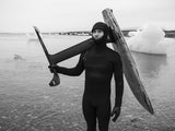 Surfer in schwarzem Neoprenanzug trägt Surfboard am Strand, Schwarz-Weiß-Fotografie