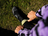 Schwarze Laufschuhe mit gelbem Detail, getragen bei Outdoor-Training auf Rasen, Draufsicht mit violettem Sportgewand sichtbar
