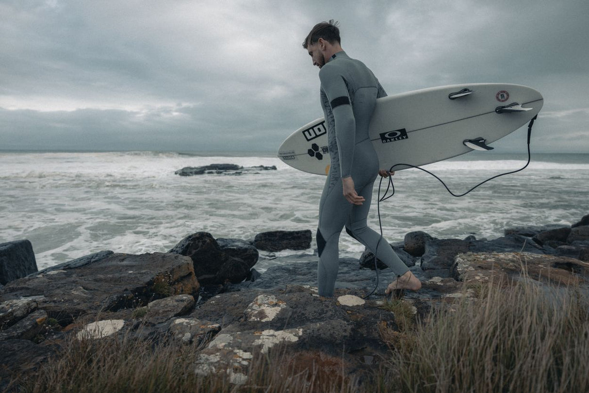 ION Seek Core 2026 Kiteboard, grau, mit Surfer in Neoprenanzug am Strand, Seitenansicht