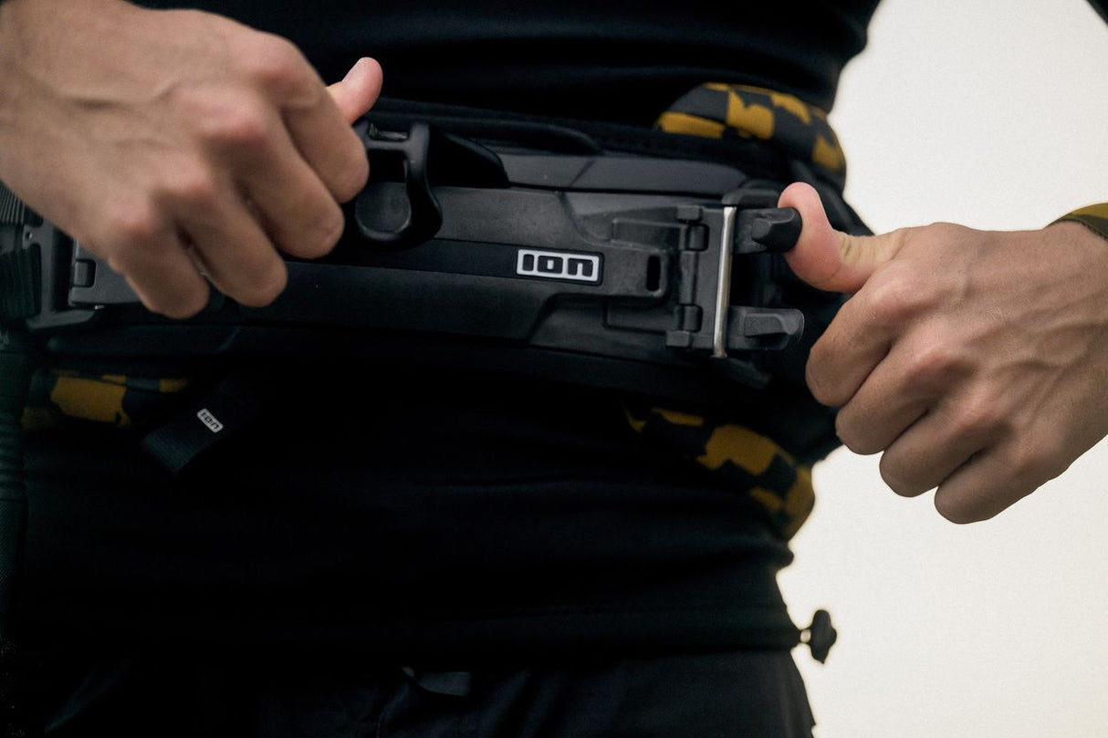 ION Riot Curv 2026 Kiteboard Weste schwarz mit gelben Details, Frontalansicht mit Händen beim Verschließen der Gurte
