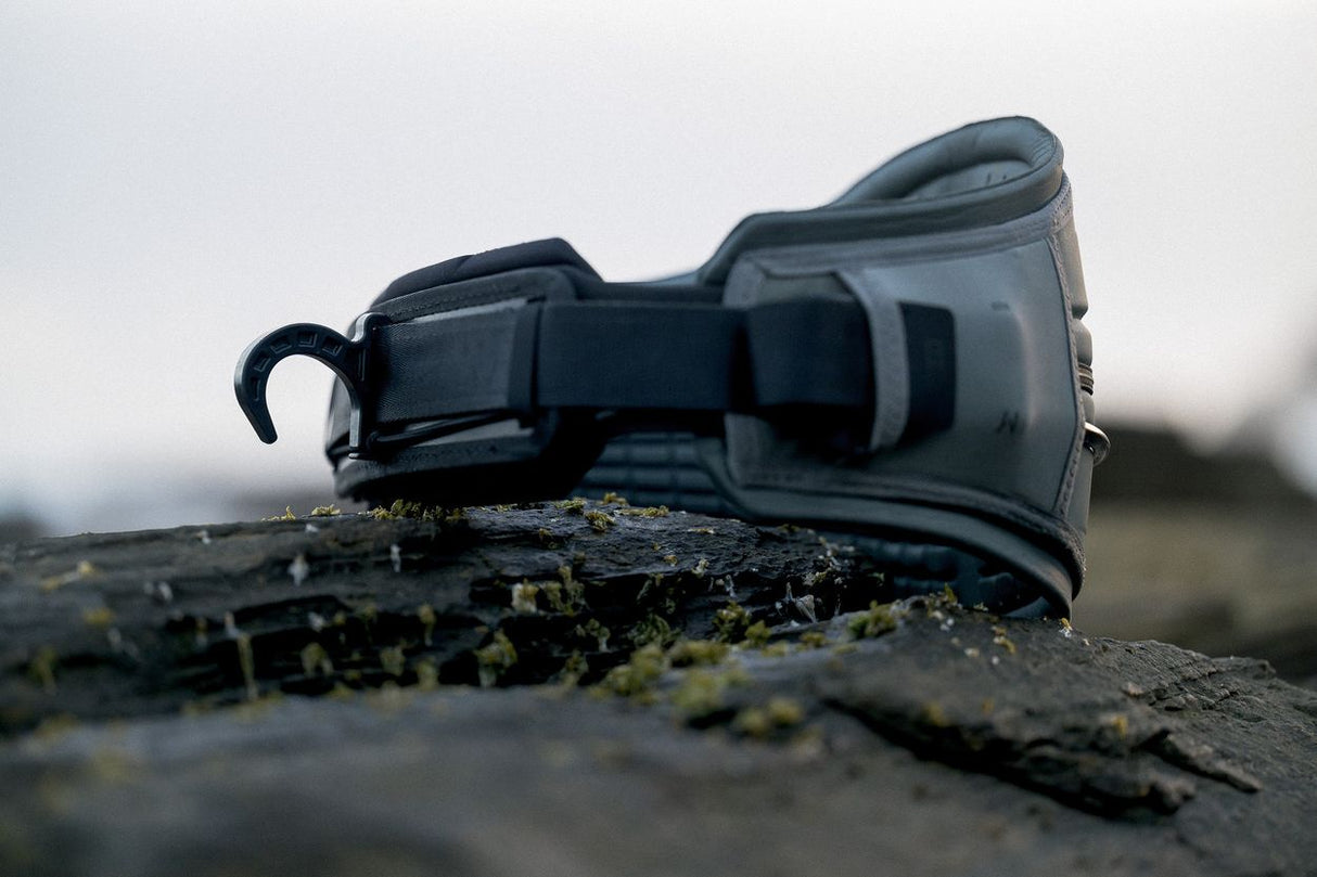 ION Rave 2026 Kiteboarding Trapez in Schwarz, Seitenansicht auf Stein, robustes Design mit Verschlüssen
