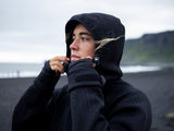 ION Neo Shelter Jacket 2024 schwarze Windjacke mit Kapuze, seitliches Porträt, Outdoor-Look am Strand