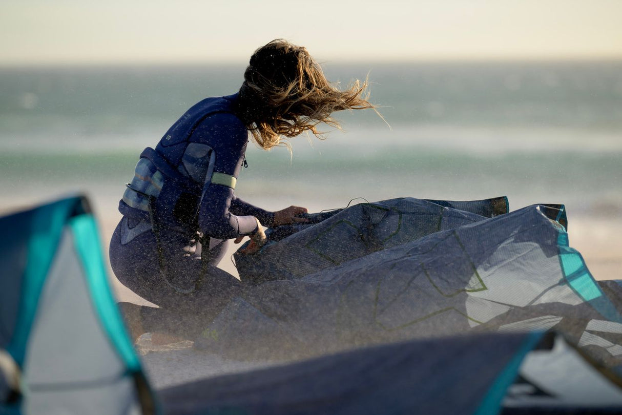 ION Sol Curv 2026 Kite in Blau und Türkis, Sportler beim Kitesurfing am Strand mit Meer im Hintergrund