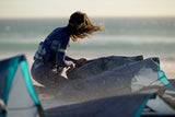 ION Sol Curv 2026 Kite in Blau und Türkis, Sportler beim Kitesurfing am Strand mit Meer im Hintergrund