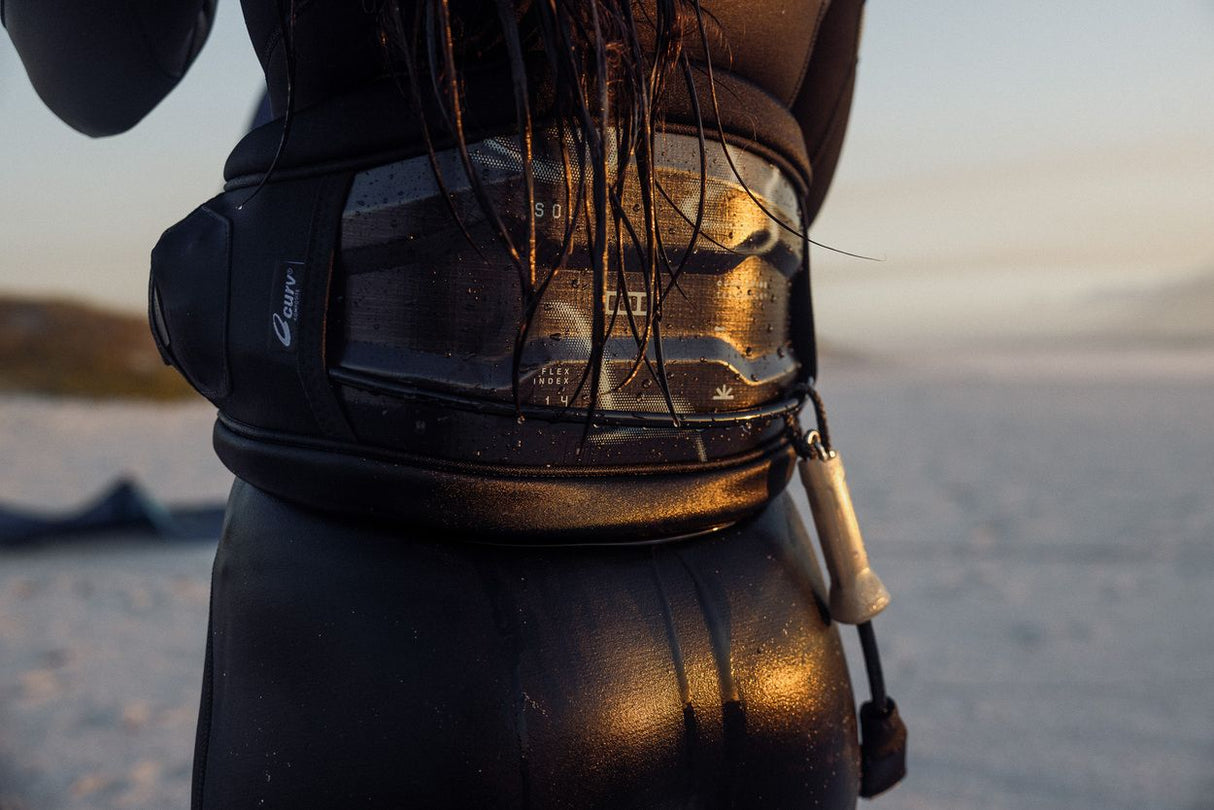 ION Sol Curv 2026 Kiteboard schwarz mit Riemen, Detailansicht in goldener Abendsonne am Wasser