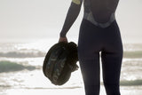 ION Sol Curv 2026 Kiteboardschuh schwarz, Nahaufnahme in Hand am Strand mit Wellen im Hintergrund