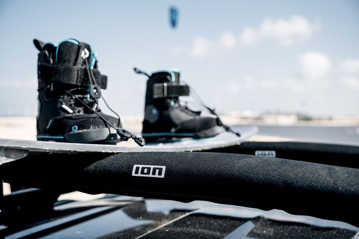 ION Roof Rack Pads 2026, schwarz mit Polsterung, auf Autodach montiert, Nahaufnahme mit Kiteausrüstung im Hintergrund