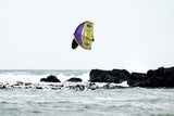 ION Wing / SUP Leash Core Coiled Hip 2024, gelb-violette Kitewing über Meer mit Felsen, Seitenansicht