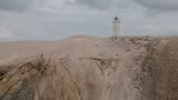 ION Neo Bommel Beanie 2026 Strickmütze in Grau, Frontansicht auf sandiger Dünenlandschaft mit Leuchtturm