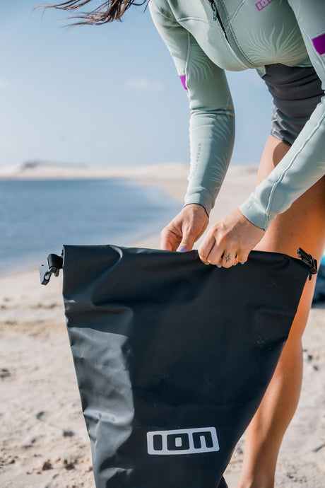 ION Dry Bag 2026 schwarz, wasserdichte Tasche mit Rollverschluss, am Strand in Händen gehalten
