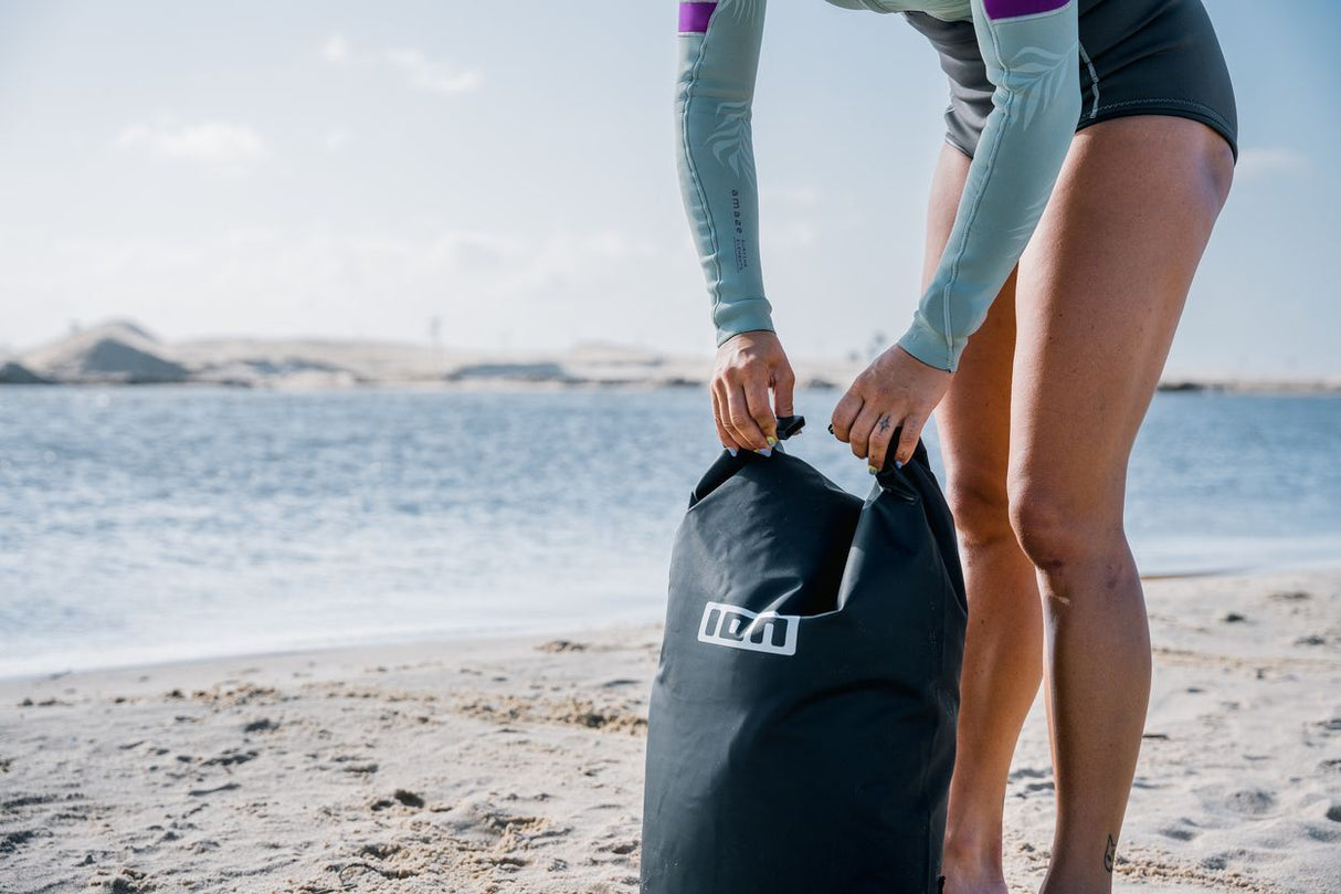 ION Dry Bag 2026 schwarze Packtasche, von Person am Strand gehalten, wasserdichte Ausführung für Wassersport