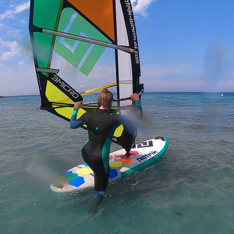 Patrik E-Ride Windsurfboard mit grünem, orangefarbenem und gelbem Segel, Fahrer im Wasser von vorne, Meerperspektive