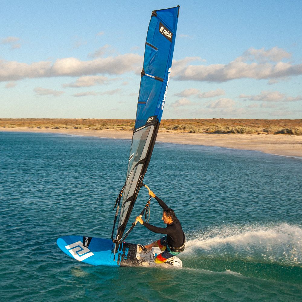 Patrik F-Ride Kiteboard blau mit Segel, Sportler in Aktion im Wasser, Strand im Hintergrund