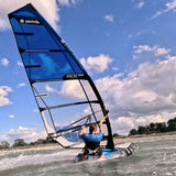Patrik Foil Ride Windsurfboard blau mit Segel, Fahrer im Wasser beim Foilen, Seitenansicht
