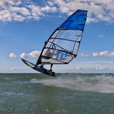 Patrik Ride Foil Windsurfboard blau schwarz in Aktion auf dem Wasser mit Welle und Himmel