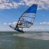 Patrik Foil Ride Windsurfboard blau-schwarz in Aktion auf dem Wasser, seitliche Ansicht mit Segel und Boom