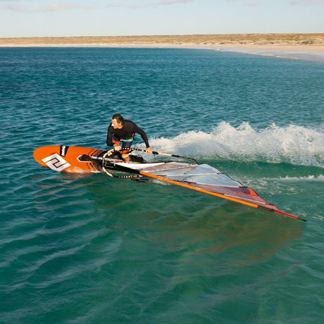 Patrik F-Race Windsurf-Board orange-schwarz im Wasser, Fahrer in Aktion mit Segel, Meereswellen im Hintergrund