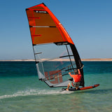 Patrik F-Race Windsurfboard rot mit Segel im Wasser, Seitenansicht am Strand