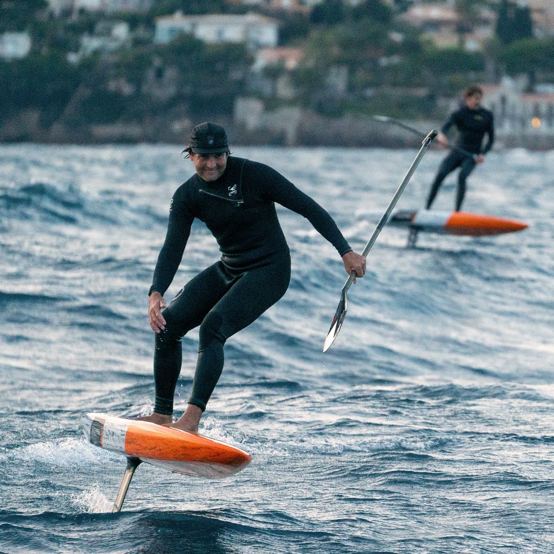 Chase DW-X Downwind SUP Board orange-schwarz, Athlet in Neoprenanzug beim Downwind-Paddeln auf Wasser