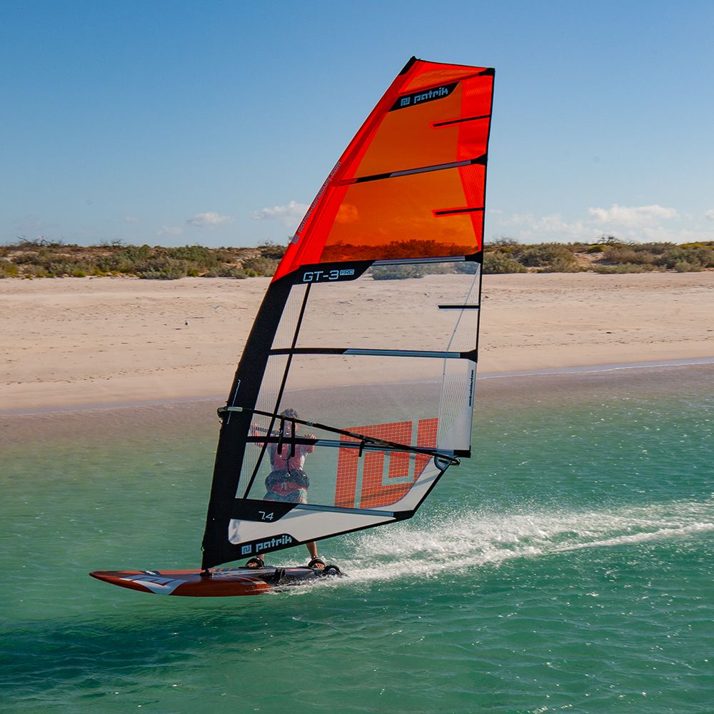 Patrik GT-3 FRC Windsurfboard rot mit Segel im Wasser, Seitenansicht am Strand