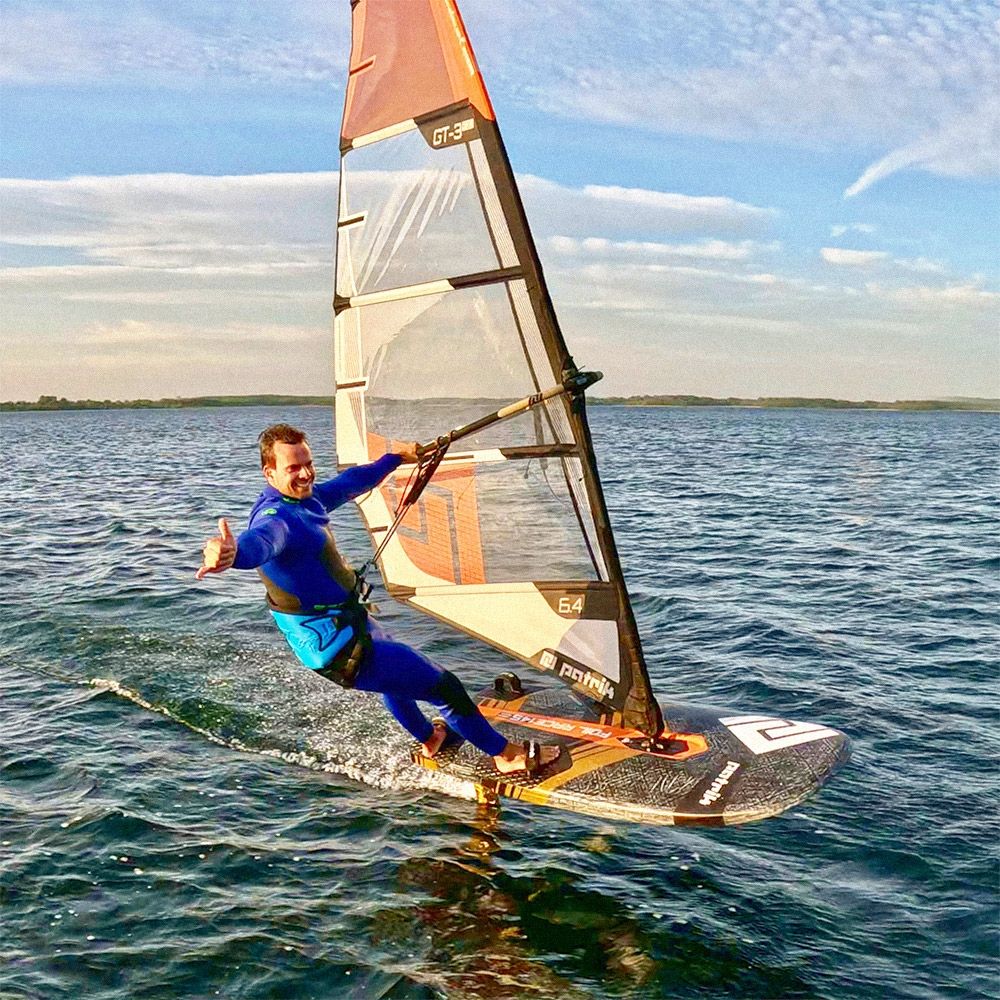 Patrik GT-3 Foil Windsurfboard mit orangeweißem Segel, Fahrer in blauem Neoprenanzug auf dem Wasser