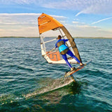 Patrik GT-3 Foil Windsurfboard mit orangem Segel, Fahrer in Aktion auf dem Wasser, Seitenansicht
