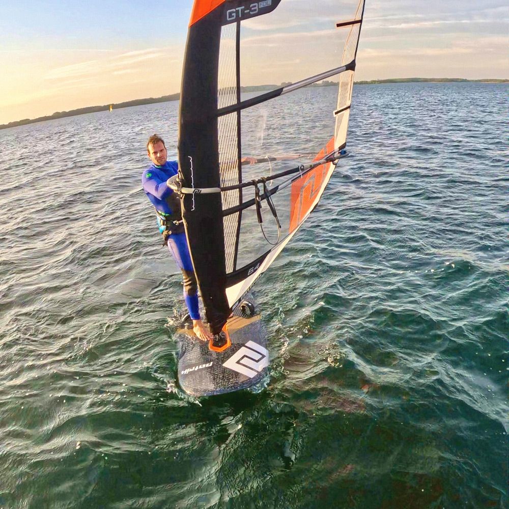 Patrik GT-3 Foil Windsurf-Board schwarz-orange mit Segel im Wasser, Frontalansicht
