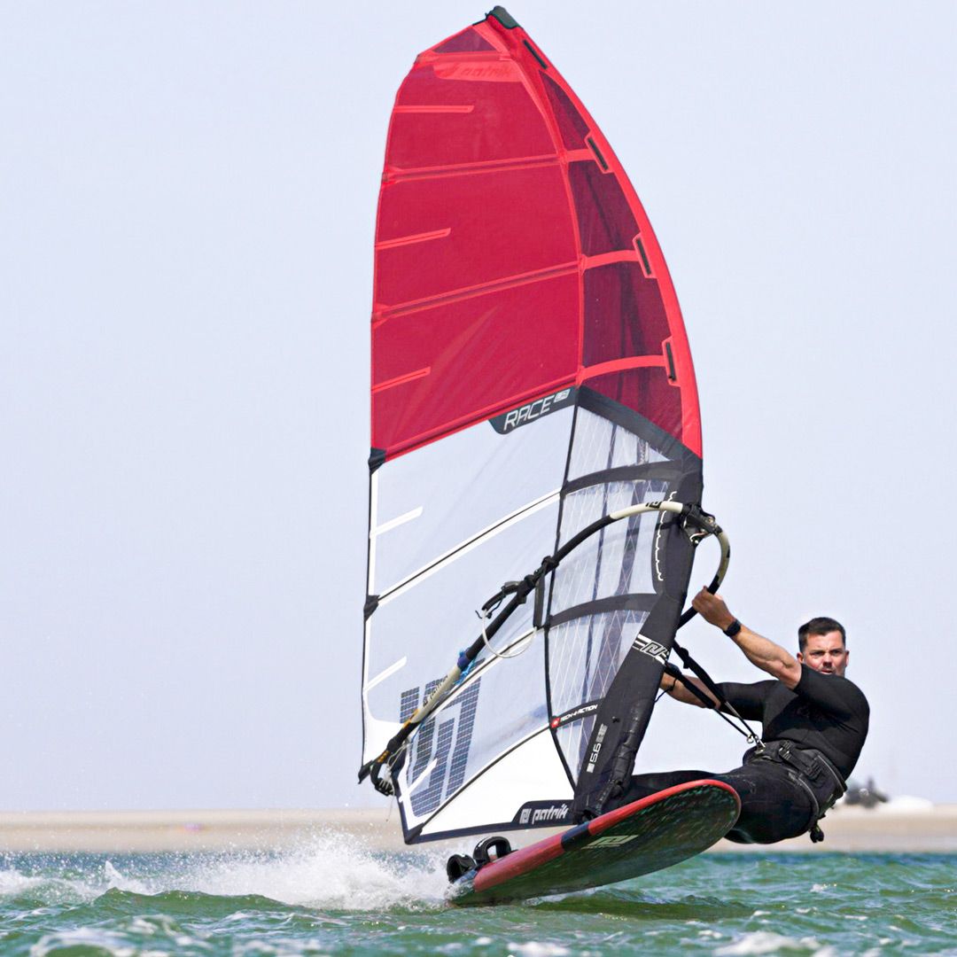 Patrik Race LA GEN2 Windsurfboard rot-weiß mit rotem Segel, Athlet in Aktion im Wasser, Seitenansicht