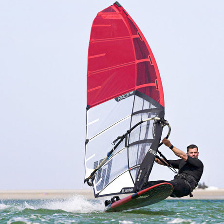 Patrik Race LA GEN2 Windsurfboard rot-weiß mit rotem Segel, Athlet in Aktion im Wasser, Seitenansicht