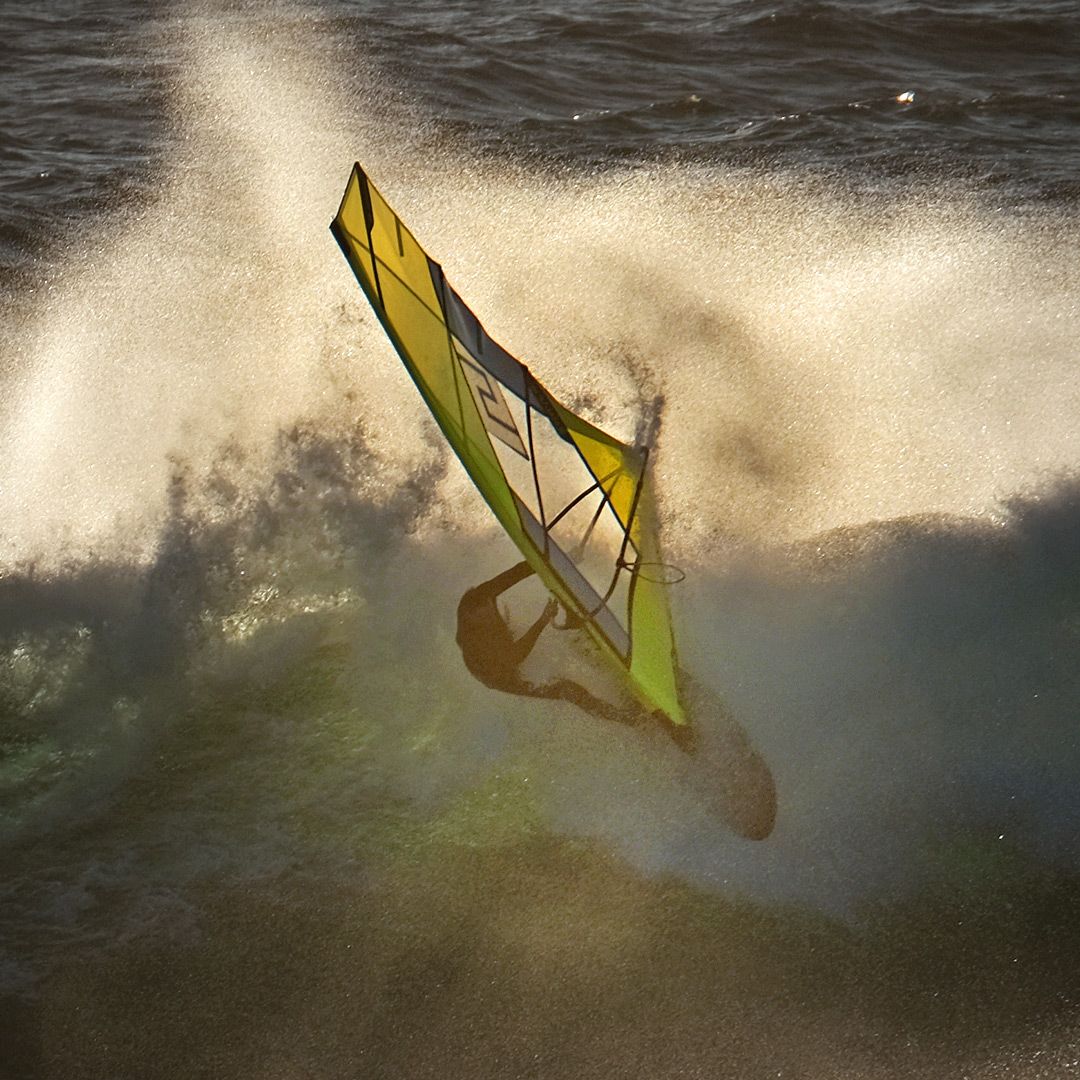 Patrik 4-Wave LTD Windsurfboard mit gelbem Segel in Aktion auf dem Wasser, dynamische Wellen im Hintergrund