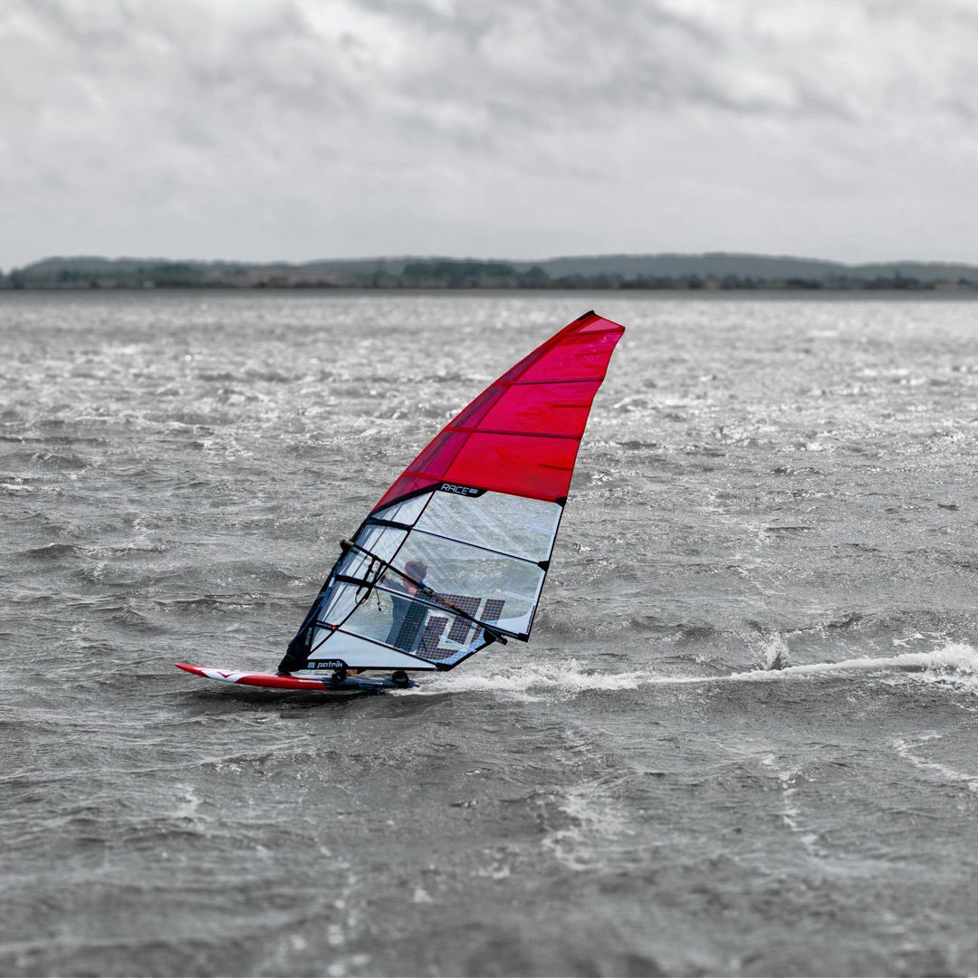 Patrik Race MA Gen2 Windsurfboard mit rotem Segel im Wasser, Seitenansicht