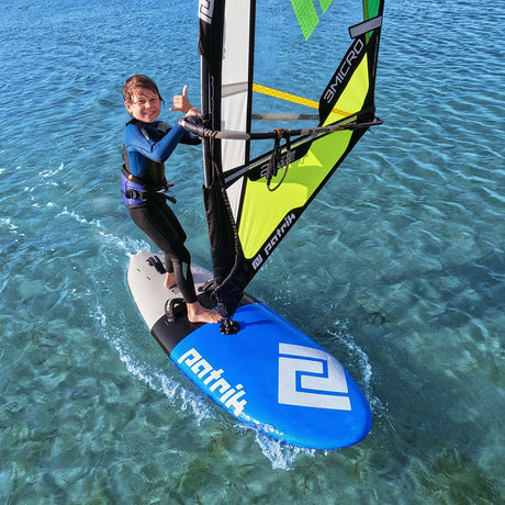 Patrik Micro Ride Windsurf-Board blau mit neongelb-grünem Segel, Kind beim Windsurfen im Wasser