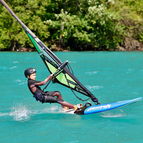 Patrik Micro Ride Windsurfboard mit grünem Segel, Kind beim Windsurfen auf türkisfarbenem Wasser in Aktion