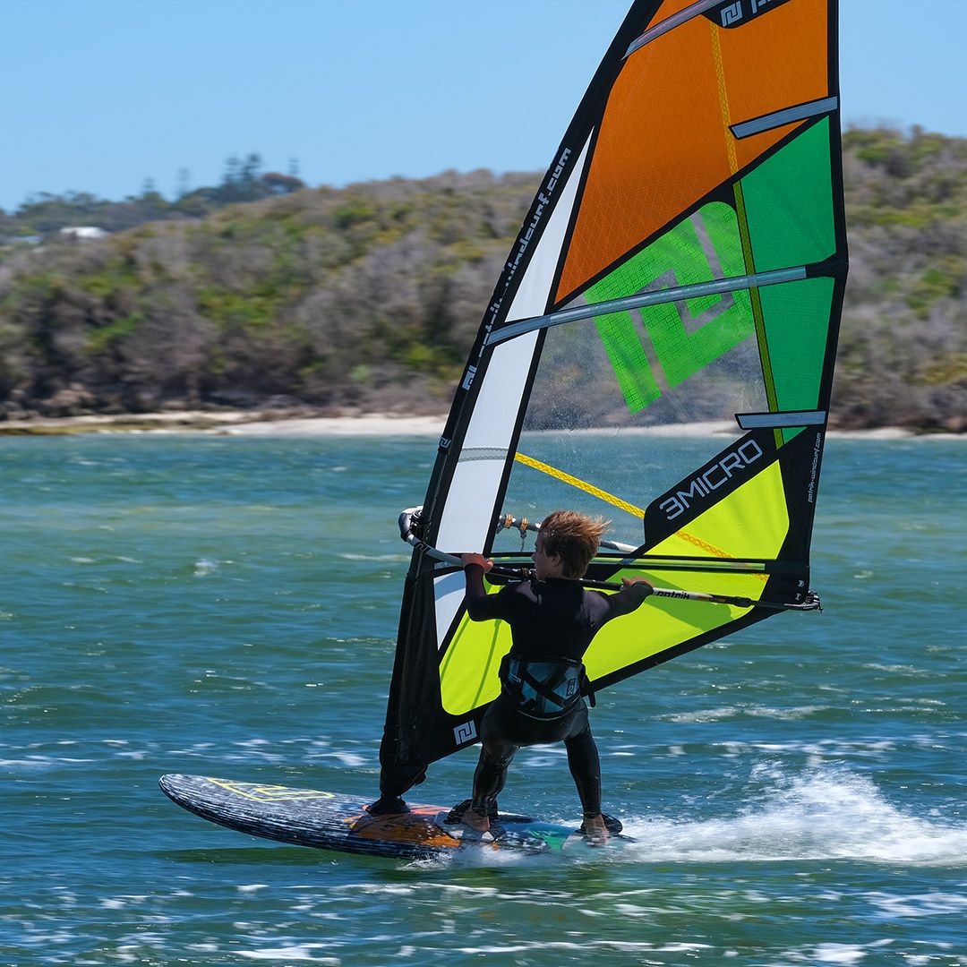 Patrik Micro-X GEN2 Windsurfboard mit orangem, grünem und gelbem Segel, Fahrer im Wasser in Aktion