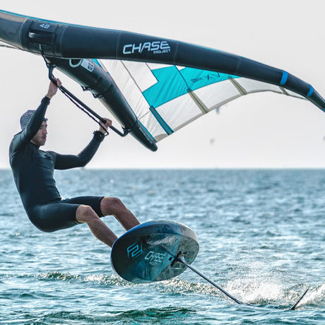 Chase WB-ML Midlength Foilboard in Türkis und Weiß, in Aktion auf dem Wasser mit Fahrer und Segel