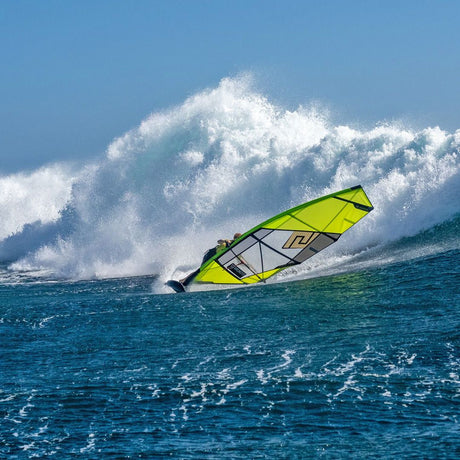 Patrik QTS-Wave Windsurfboard neongelb in Aktion auf dem Wasser mit großer Welle im Hintergrund