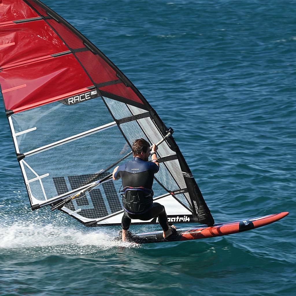 Patrik Slalom Windsurfboard rot-schwarz mit rotem Segel, Athlet in Aktion auf dem Wasser
