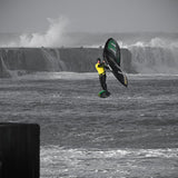 Patrik Wing V2 Volant Cross Kite in Schwarz-Grün, in Aktion über stürmischer See mit Kitesurfer in gelbem Neoprenanzug