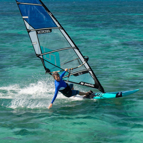 Patrik X-Cross Windsurfboard blau-weiß mit Segel im Wasser, Frontansicht beim Windsurfen