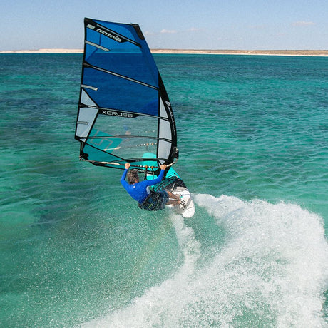 Patrik X-Cross Windsurfboard blau in Aktion auf türkisem Meer mit Wellen, Frontalansicht