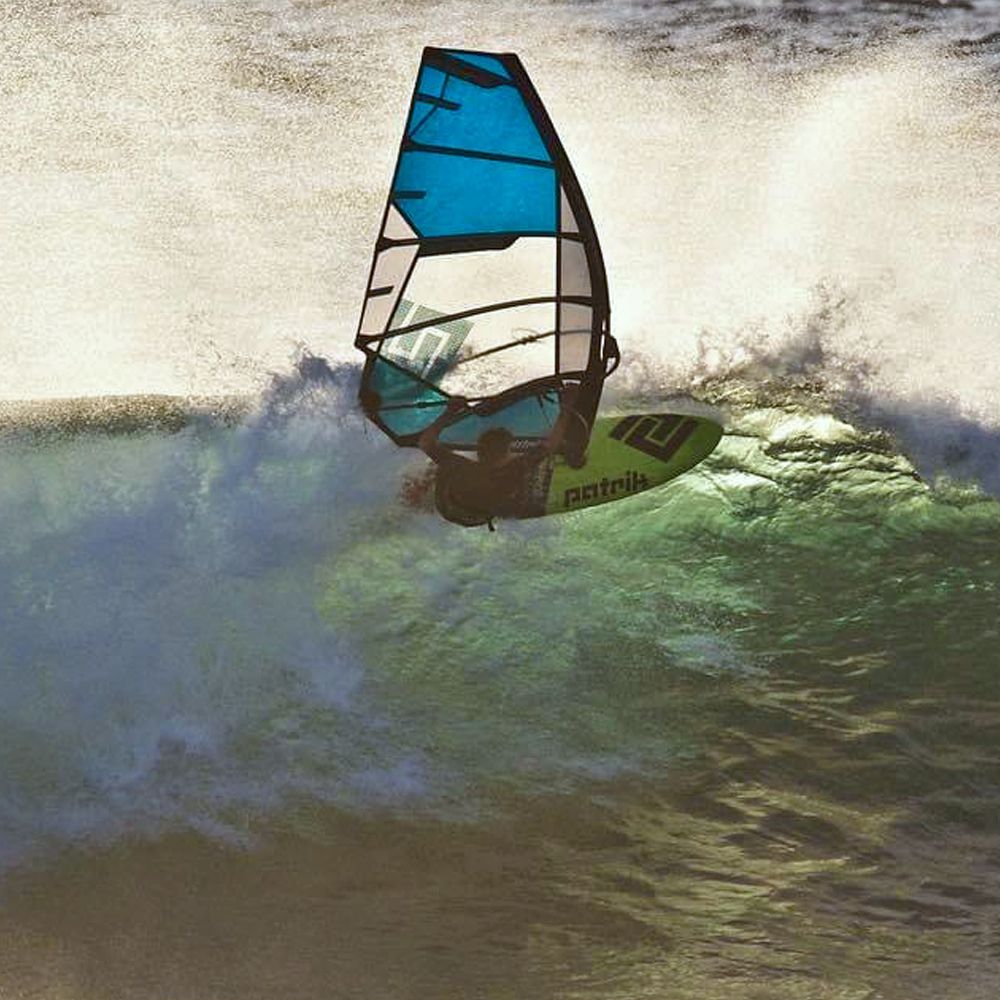 Patrik X-Cross X-Ply Windsegel blau-weiß mit schwarzem Gestänge beim Wellenritt im Wasser