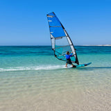 Patrik X-Cross X-Ply Windsurfboard blau mit schwarzem Mast im Wasser, Frontalansicht beim Windsurfen